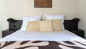 A neatly made bed with white linens and a patterned throw, flanked by two bedside tables with lamps, against a plain wall with a geometric artwork. - Elegant City Room near Antwerp Cathedral (Antwerpen)