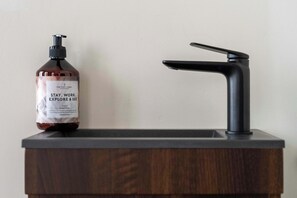 Ein Badezimmer mit einem dunklen Holzwaschtisch, einem schwarzen Wasserhahn und einer Handdesinfektionsmittel-Flasche.