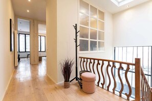 Ein Flur mit Holzboden, einer Treppe mit Holzgeländer, einem großen Fenster mit Sandstrahlglas und einer Pflanze in einem gewobenen Korb.