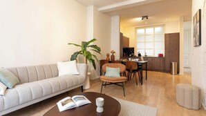 Een woonkamer met een bank, een salontafel, een eethoek met stoelen, een plant en een keuken op de achtergrond.