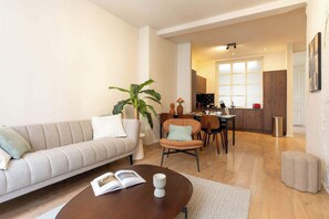 Una sala de estar con sofá, mesa de centro, comedor con sillas, una planta y una cocina al fondo.