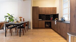 Een moderne keuken met houten kastjes, een zwart aanrecht en een eethoek met een tafel en stoelen.