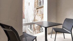 Een balkon met een tafel en twee stoelen, met uitzicht op een bakstenen gebouw en een raam.