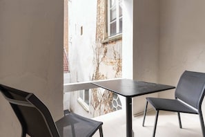 Un balcón con una mesa y dos sillas, vista a un edificio de ladrillo y una ventana.