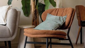 Een moderne woonkamer met een bruine fauteuil, een grijze fauteuil, een witte bank en een grote groene plant.