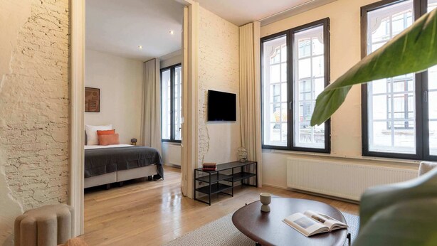 Een moderne hotelkamer met een bed, een televisie, een tafeltje en grote ramen.