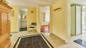 A hallway with a wooden cabinet, a chair, and a kitchen in the background. - Villa Luna – Stylish Living. Arrive feeling relaxed. Feel at home. (Schaafheim)