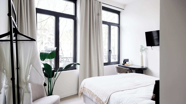 Ein modernes Schlafzimmer mit Bett, Schreibtisch, Stuhl, einer Pflanze und einem Fenster mit Vorhängen.