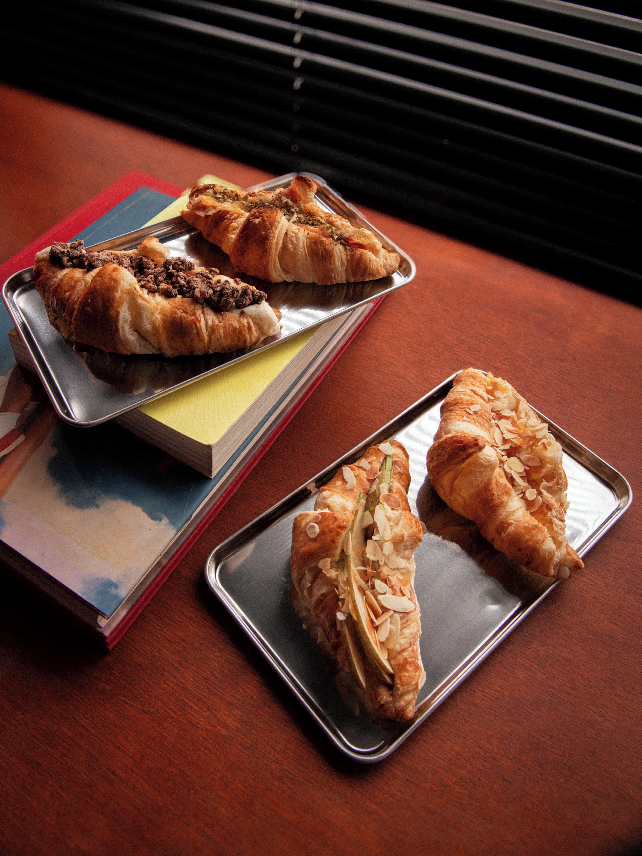 Trois plateaux en métal garnis de pâtisseries, posés sur une table en bois.