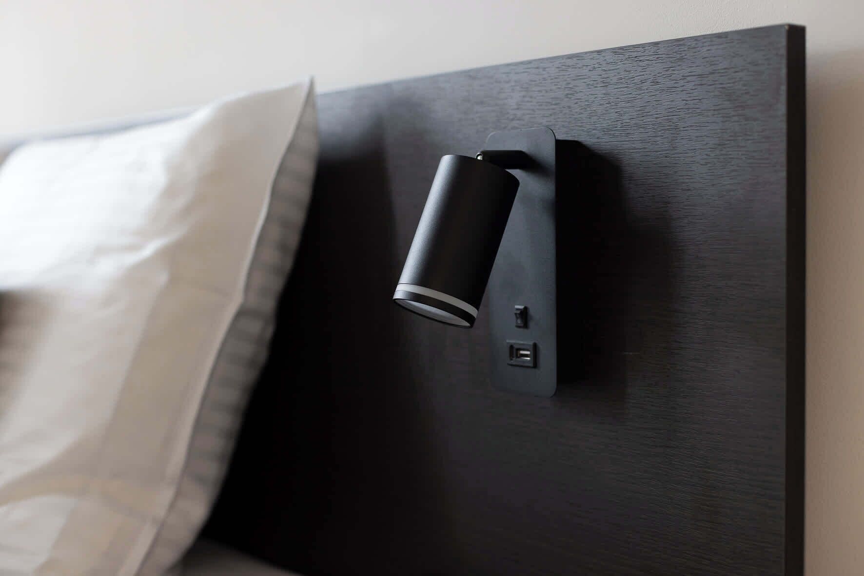 A modern bed with a black headboard, a white pillow, and a bedside control panel.