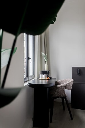 A small, modern room with a round table, a chair, a window with curtains, a potted plant, and a black cabinet. - ROMY | Stylish Stay in the Heart of Antwerp (Antwerpen)