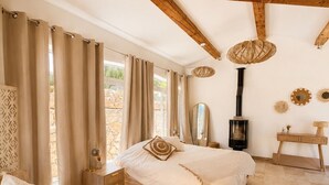 A bedroom with a bed, bedside tables, a chair, a woven rug, a mirror, a hanging light fixture, and a fireplace. - Luxury Villa for 12 Guests with Heated Pool in St. Maxime, La Nartelle Private Estate (Sainte-Maxime)