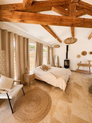 A bedroom with a bed, bedside tables, a chair, a woven rug, a mirror, a hanging light fixture, and a fireplace. - Luxury Villa for 12 Guests with Heated Pool in St. Maxime, La Nartelle Private Estate (Sainte-Maxime)