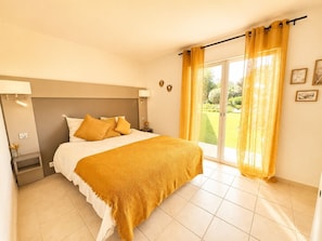 A bedroom with a bed, a nightstand, a lamp, a window with curtains, and a view of the outdoors. - Luxury Villa for 12 Guests with Heated Pool in St. Maxime, La Nartelle Private Estate (Sainte-Maxime)