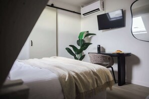 A bedroom with a bed, a bedside table, a plant, a TV, and an air conditioning unit. - ROMY | Cozy Top-Floor Room in Central Antwerp (Antwerpen)