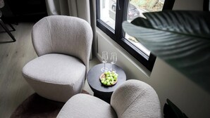 Ett mysigt rum med ett stort fönster, en säng, ett runt bord med en skål med vindruvor och två glas, och två bekväma fåtöljer.