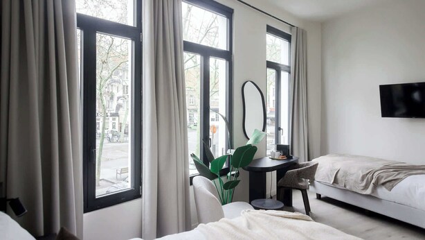 Ett hotellrum med två sängar, ett skrivbord med en stol, en TV och stora fönster med gardiner.