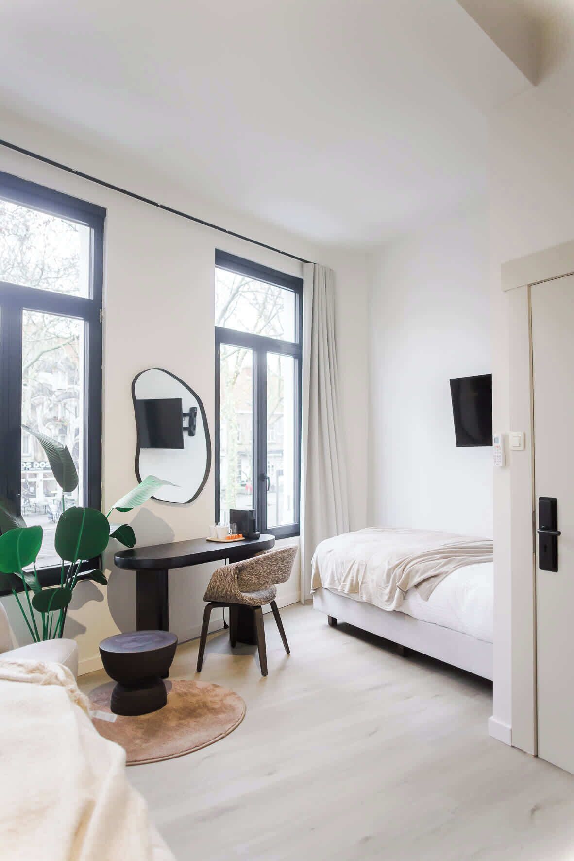 A modern bedroom with a bed, desk, chair, and large windows.