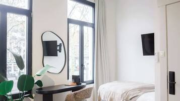 A modern bedroom with a bed, desk, chair, and large windows.