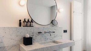 A modern bathroom with a marble sink, a round mirror, and a towel rack. - Riga Suites | Deluxe Double Room with Bath (Antwerpen)