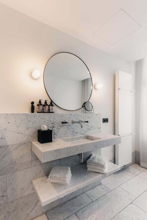 Un baño moderno con lavamanos de mármol, un espejo redondo y un perchero.