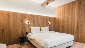 A bedroom with a wooden wall, a bed with white bedding, a small round table, and a black floor lamp.