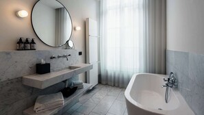 A modern bathroom with a marble sink, a large mirror, a bathtub, and a window with sheer curtains.
