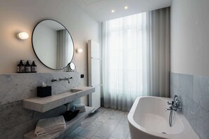 A modern bathroom with a marble sink, a large mirror, a bathtub, and a window with sheer curtains.