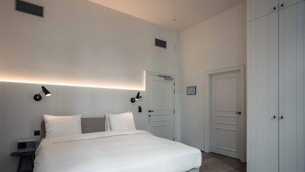 A modern bedroom with a large bed, bedside lamps, a wardrobe, and a small table with a radio. - Riga Suites | Deluxe Double Room with Bath (Antwerpen)