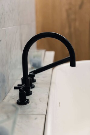 A bathroom with a white bathtub, a black faucet, and a marble wall.