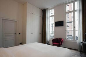 Una habitación de hotel con una cama, una silla roja, un televisor y ventanas amplias.