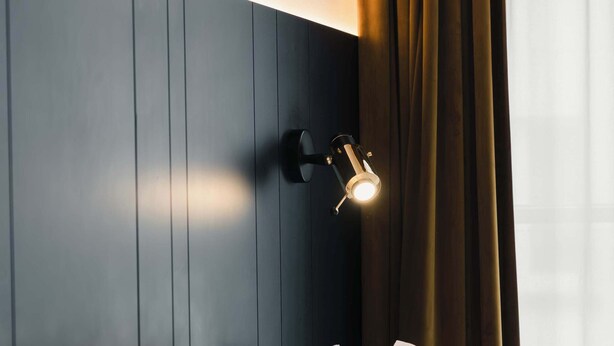 A hotel room with a dark headboard, a bedside lamp, and a window with curtains. - Riga Suites | Duplex Room with Private Terrace (Antwerpen)