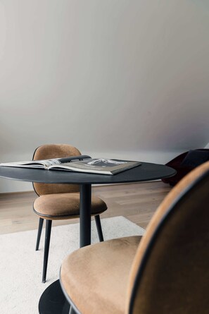 Una mesa redonda con una revista, una silla y un bolso rojo en una habitación con pared blanca y suelo de madera.