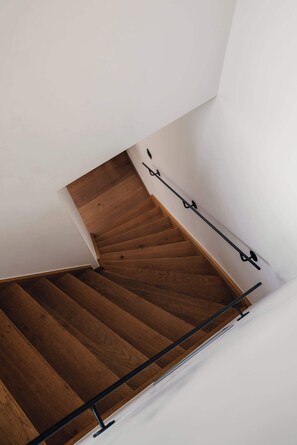 Una escalera de madera con barandales negros, paredes blancas y piso de madera.