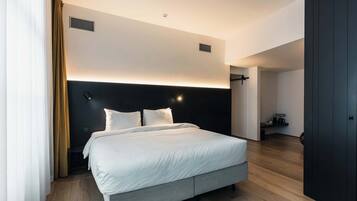Una habitación de hotel moderna con una cama grande, un cabecero oscuro y suelo de madera.