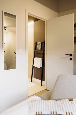 A hotel room with a bed, a mirror, a towel rack, and a door leading to a bathroom. - Charming Roof-Top Apartment in Antwerp (Antwerpen)