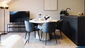 Een moderne woonkamer met een flatscreen televisie, een eettafel met stoelen, een bank en een keuken met aanrecht en spoelbak.