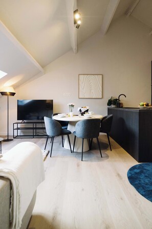 A modern living room with a flat-screen TV, a dining table with chairs, a sofa, and a kitchen area with a countertop and sink. - Charming Roof-Top Apartment in Antwerp (Antwerpen)