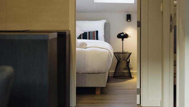 Een slaapkamer met dakraam, een bedlamp en uitzicht op een gang.