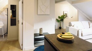 Een moderne woonruimte met een keukenhoek, een eettafel met borden, een blauw vloerkleed en een witte bank.