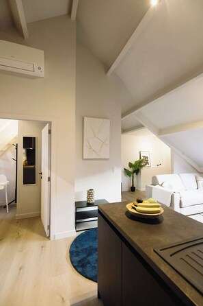 A modern living space with a kitchen area, a dining table with plates, a blue rug, and a white sofa. - Charming Roof-Top Apartment in Antwerp (Antwerpen)