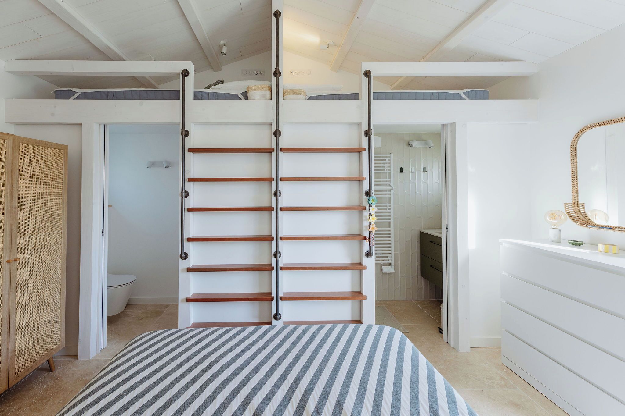 A bedroom with a bunk bed, a wooden ladder, a striped bedspread, a dresser, and a mirror.