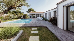 Ein modernes Haus mit Swimmingpool, Holzterrasse und Garten mit verschiedenen Pflanzen.