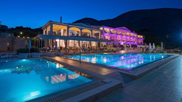 A hotel with a swimming pool, outdoor seating, and a mountain backdrop. - Odyssey Hotel (Kefalonia)