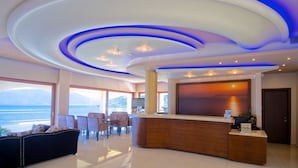 A hotel lobby with a reception desk, seating area, and large windows offering a view of the sea. - Odyssey Hotel (Kefalonia)