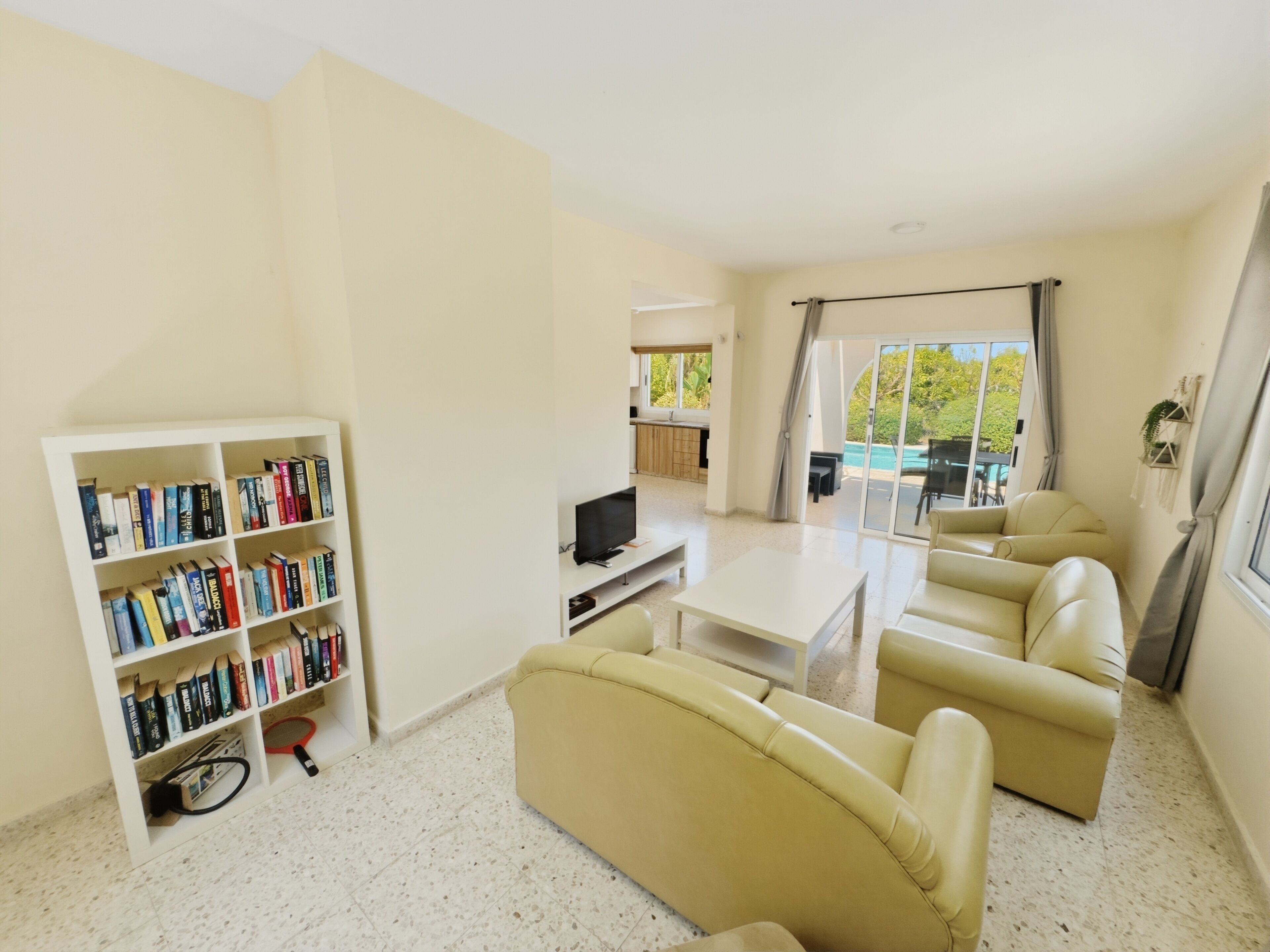 A spacious living area with a sofa set, a television, a bookshelf, and a sliding glass door leading to a balcony.