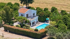 Una villa bianca con piscina, immersa nel verde e alberi.