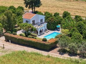 Eine weiße Villa mit Swimmingpool, umgeben von viel Grün und Bäumen.
