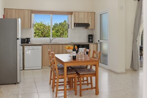 Eine moderne Küche mit Holzausstattung, einem Esstisch mit Stühlen, einem eingebauten Backofen und einem Fenster mit Blick auf Grünflächen.