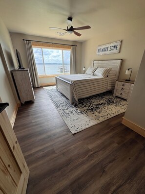 A bedroom with a bed, a nightstand, a lamp, a ceiling fan, a window with curtains, and a 'NO WAKE ZONE' sign. - Lake Daze . (Fort Gaines)